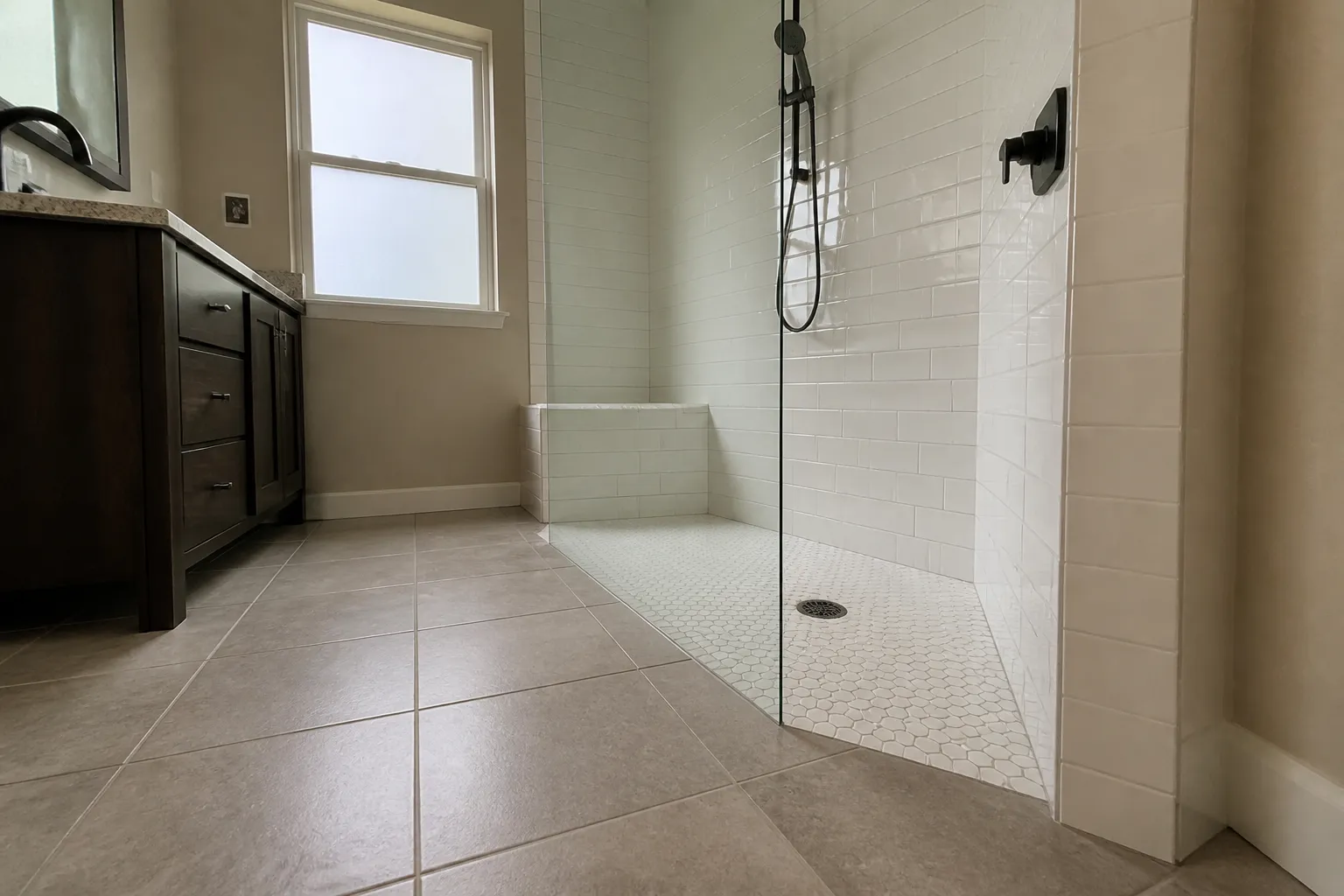 Low-angle view of a curbless walk-in shower entry, mosaic pan, tiled bench, and handheld shower on a slide bar